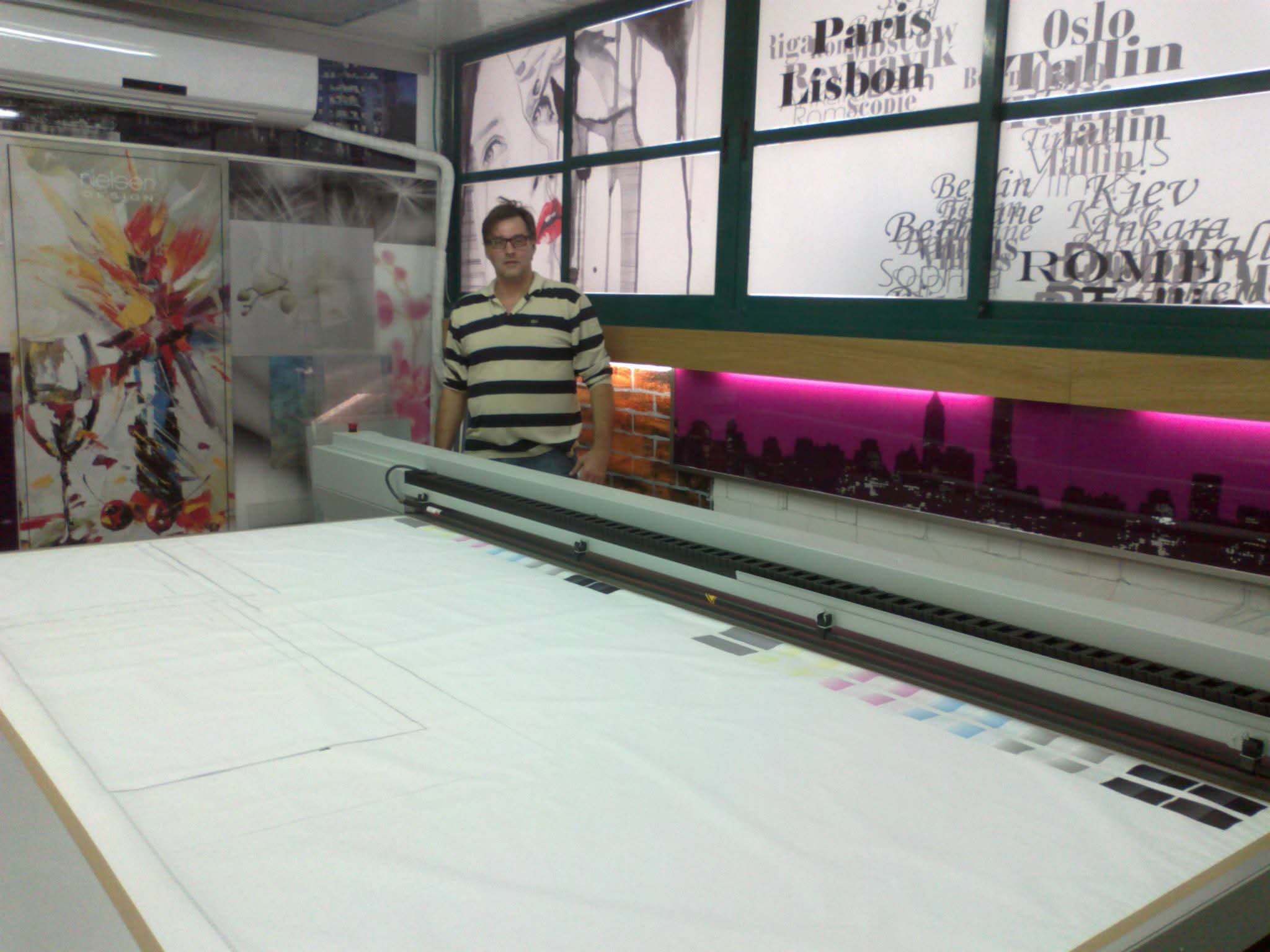 A person stands beside a large printing machine and worktable in the workshop.